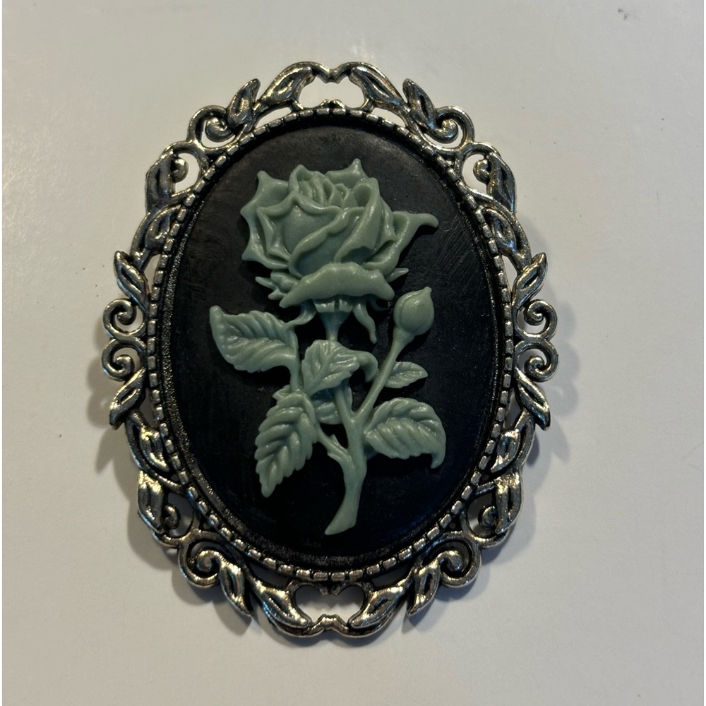 Gorgeous oval brooch green rose on black background surrounded by silver color